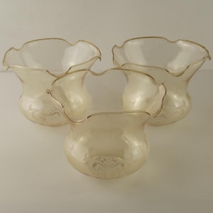 May include: Three clear glass vases with a ruffled rim and gold trim. The vases have a pearlescent finish and a decorative floral pattern near the base. The vases are arranged in a triangular formation.