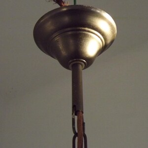 Peut inclure: Gros plan d'une rosace de plafond de couleur bronze avec une tige centrale et une cha&icirc;ne. La rosace a une forme arrondie en forme de cloche et une finition m&eacute;tallique chaude. La cha&icirc;ne est de couleur marron fonc&eacute;.