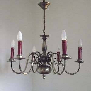 Peut inclure: Un lustre en laiton vintage &agrave; six bras, chacun tenant une lumi&egrave;re rouge en forme de bougie. Le lustre a un corps central et est suspendu &agrave; une cha&icirc;ne. Les ampoules sont blanches.