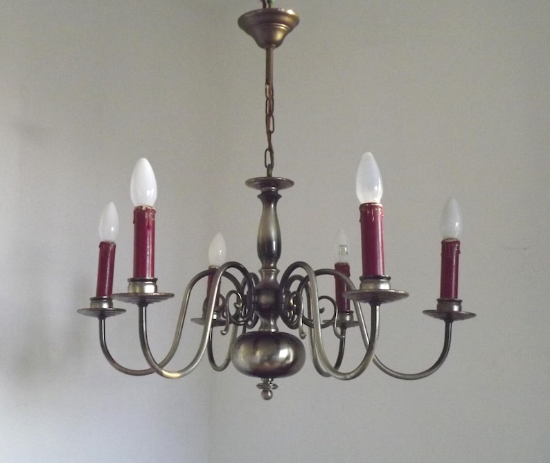 Peut inclure: Un lustre en laiton vintage &agrave; six bras, chacun tenant une lumi&egrave;re rouge en forme de bougie. Le lustre a un corps central et est suspendu &agrave; une cha&icirc;ne. Les ampoules sont blanches.