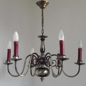 Peut inclure: Un lustre vintage &agrave; six lumi&egrave;res. Le luminaire a une finition m&eacute;tallique avec des bras incurv&eacute;s tenant des ampoules rouges en forme de bougie. Les ampoules sont surmont&eacute;es d'ampoules blanches en forme de goutte d'eau. Le lustre est suspendu &agrave; une cha&icirc;ne.