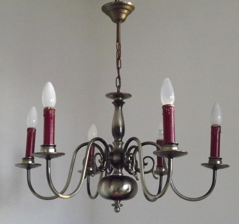Peut inclure: Un lustre vintage &agrave; six lumi&egrave;res. Le luminaire a une finition m&eacute;tallique avec des bras incurv&eacute;s tenant des ampoules rouges en forme de bougie. Les ampoules sont surmont&eacute;es d'ampoules blanches en forme de goutte d'eau. Le lustre est suspendu &agrave; une cha&icirc;ne.
