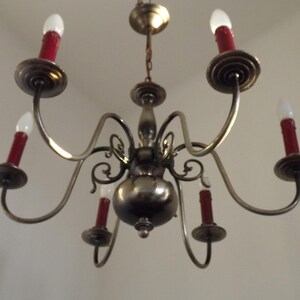 Peut inclure: Un lustre ancien avec six bras courb&eacute;s, chacun portant une ampoule rouge en forme de bougie. Le luminaire a une finition m&eacute;tallique et est suspendu au plafond. Le design est orn&eacute; et classique, pour l'&eacute;clairage int&eacute;rieur.