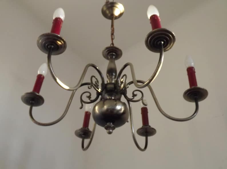 Peut inclure: Un lustre ancien avec six bras courb&eacute;s, chacun portant une ampoule rouge en forme de bougie. Le luminaire a une finition m&eacute;tallique et est suspendu au plafond. Le design est orn&eacute; et classique, pour l'&eacute;clairage int&eacute;rieur.