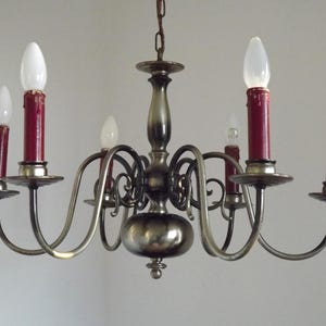Peut inclure: Un lustre vintage avec six lumi&egrave;res en forme de bougie. Le lustre a une finition m&eacute;tallique avec des bras incurv&eacute;s tenant des bougeoirs rouges et des ampoules blanches. Un luminaire d&eacute;coratif.