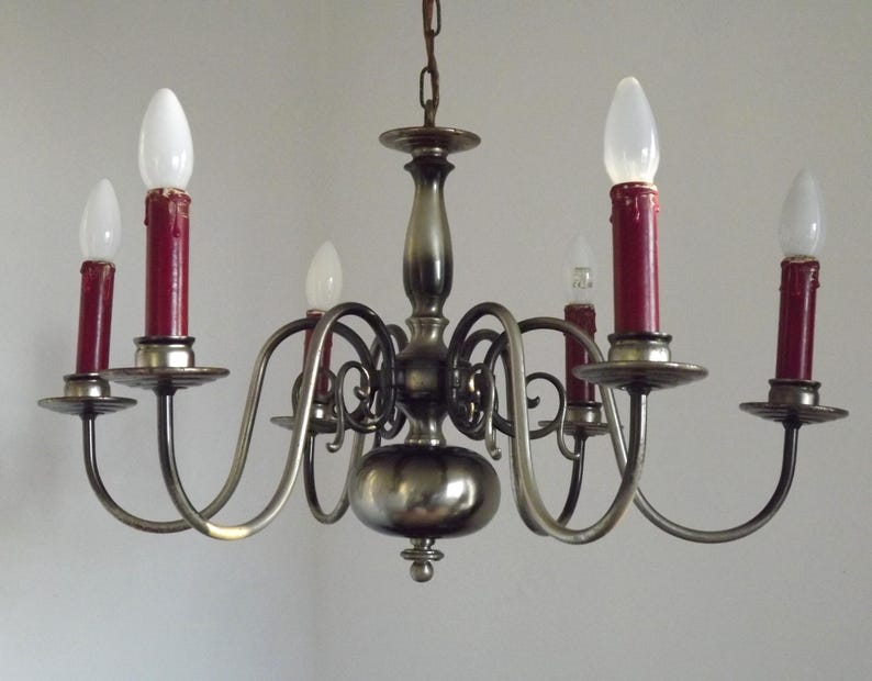 Peut inclure: Un lustre vintage avec six lumi&egrave;res en forme de bougie. Le lustre a une finition m&eacute;tallique avec des bras incurv&eacute;s tenant des bougeoirs rouges et des ampoules blanches. Un luminaire d&eacute;coratif.