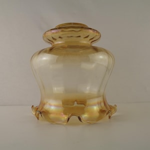 Op de afbeelding: Een vintage glazen lampenkap met een geschulpte rand. De kap heeft een uitlopende, klokvormige vorm en een warme, amberkleurige tint met goud en paars iriserend. Het glas is helder.
