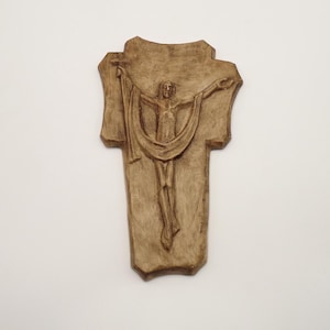 May include: A wooden wall plaque depicting a carved image of Jesus Christ on a cross. The figure is depicted with arms outstretched and a cloth draped over the body.