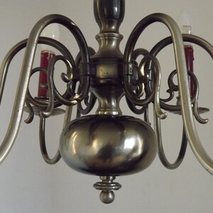 Peut inclure: Gros plan sur un lustre vintage avec une finition m&eacute;tallique. Le luminaire a des bras incurv&eacute;s, des volutes d&eacute;coratives et des bougeoirs avec des bougies rouges. Le corps central est de forme arrondie.