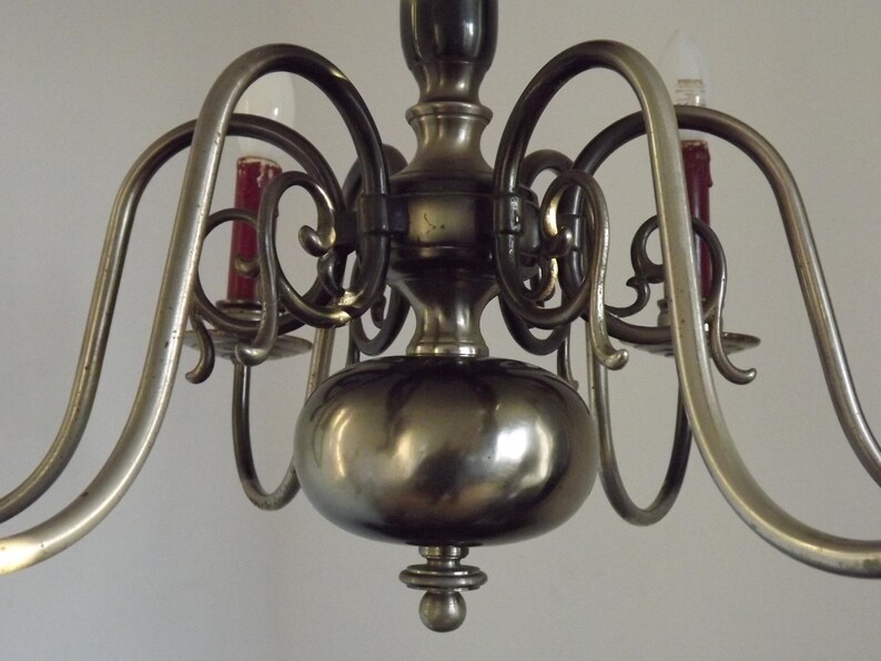 Peut inclure: Gros plan sur un lustre vintage avec une finition m&eacute;tallique. Le luminaire a des bras incurv&eacute;s, des volutes d&eacute;coratives et des bougeoirs avec des bougies rouges. Le corps central est de forme arrondie.