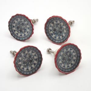 Op de afbeelding: Set van vier keramische kastknoppen. Elke knop heeft een blauw-wit bloemmotief met een rode, geschulpte rand. Ze hebben een zilveren metalen schroef voor bevestiging.