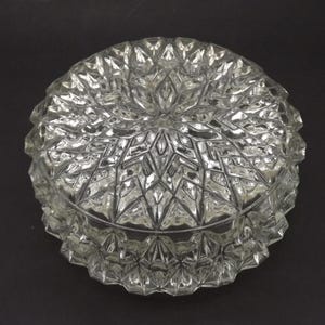 May include: A clear glass bowl with a detailed geometric pattern. The bowl has a rounded shape with a textured surface, reflecting light. The design features diamond and star shapes, creating a decorative effect. The bowl is likely for decorative use.