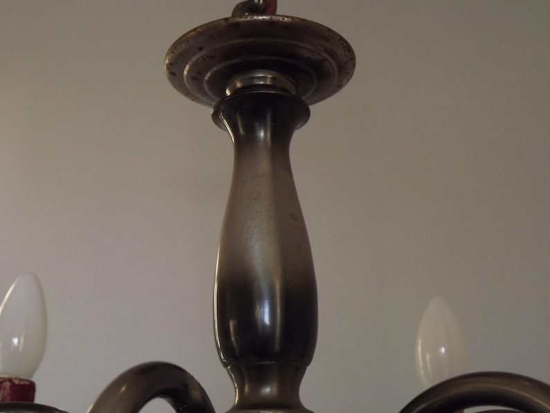 Peut inclure: Gros plan sur la colonne centrale et la plaque de montage d'un lustre vintage. Le luminaire en m&eacute;tal pr&eacute;sente une finition sombre et vieillie, avec une ampoule visible de chaque c&ocirc;t&eacute;. Le design sugg&egrave;re un style ancien ou r&eacute;tro.