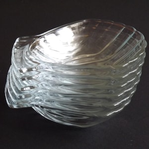Peut inclure: Une pile de six coupelles en verre transparent en forme de coquillages. Chaque coupelle présente une texture moulée et nervurée sur la surface extérieure et un intérieur lisse et concave. Le verre est transparent et reflète la lumière.