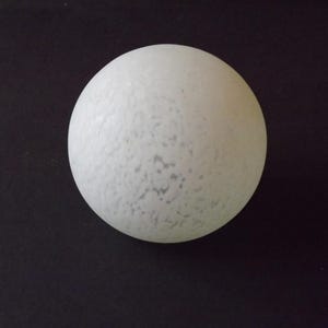 Op de afbeelding: Een witte bol met een gespikkelde textuur, tegen een donkere achtergrond. Het object heeft een matte afwerking, met subtiele kleurvariaties. De vorm is een perfecte cirkel. De textuur van de bol geeft het een unieke uitstraling.