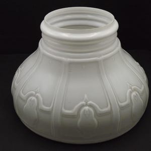 Peut inclure: Un abat-jour en verre blanc de forme arrondie et bulbeuse. L'abat-jour présente des détails côtelés verticaux et des motifs floraux en relief décoratifs. L'ouverture supérieure est cylindrique. L'abat-jour est conçu pour un luminaire.