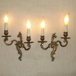 May include: A pair of ornate brass wall sconces with three candle-style light bulbs each. The sconces have a scrolled design and are finished in a warm gold tone.