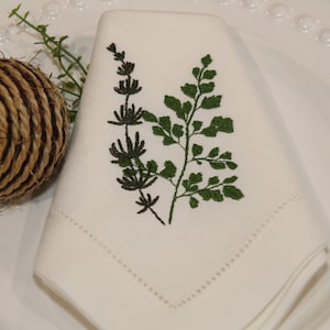 Puede incluir: Servilleta de lino blanco con un dise&ntilde;o de helecho y hojas bordadas en verde.