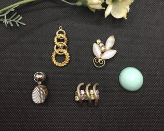 May include: Assortment of gold and silver jewelry findings, including a chain link, a leaf design, a flower design, and a round bead. The findings are on a black background.