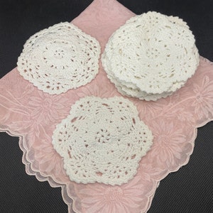 May include: A set of six white crocheted doilies, displayed on a pink floral fabric background.