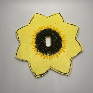 May include: A yellow wooden light switch cover with a black and yellow sunflower design.