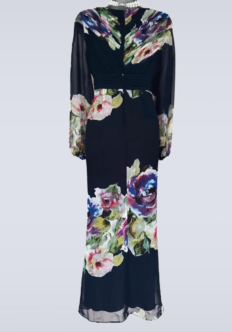 Puede incluir: Vestido largo azul marino oscuro con estampado floral. El vestido presenta mangas largas y transparentes y un corpi&ntilde;o ajustado. El estampado floral incluye flores rosas, moradas y blancas. Adecuado para ocasiones formales.