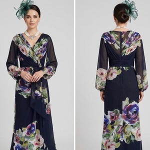 Puede incluir: Vestido formal azul marino con estampado floral, mangas largas transparentes y escote en V. El vestido presenta un corpi&ntilde;o cruzado y una falda fluida. El estampado floral incluye tonos de rosa, morado y verde. La modelo lleva un tocado verde y un collar de perlas.