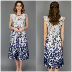 May include: A sleeveless floral print dress with a ruffled overlay. The dress features a watercolor-style floral pattern in shades of purple, blue, and white. The dress has a knee-length hemline and a fitted bodice.
