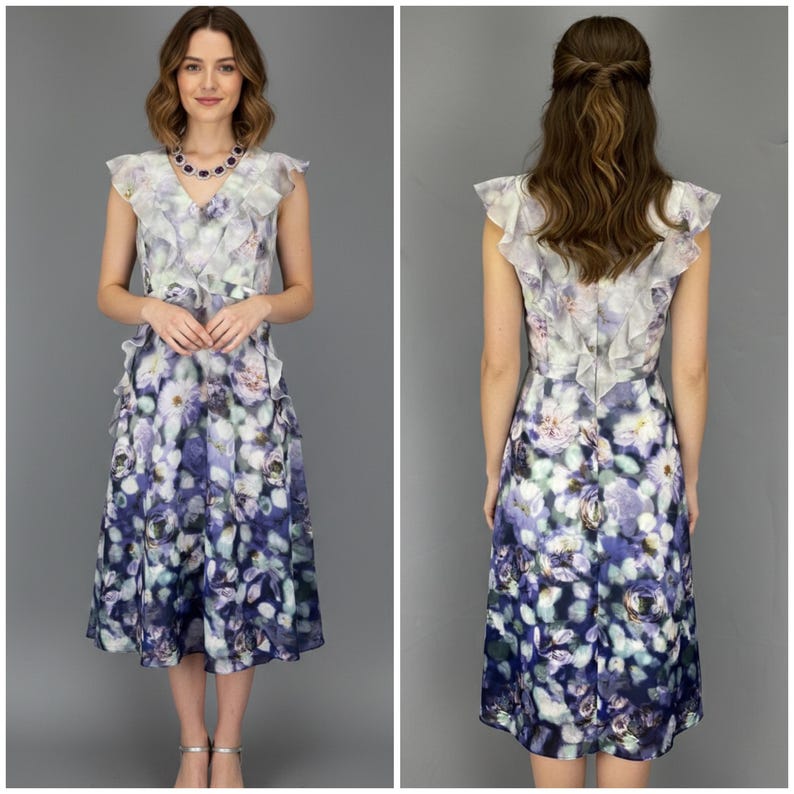 May include: A sleeveless floral print dress with a ruffled overlay. The dress features a watercolor-style floral pattern in shades of purple, blue, and white. The dress has a knee-length hemline and a fitted bodice.