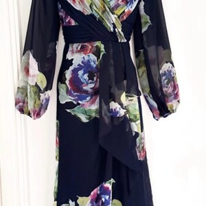 Puede incluir: Vestido largo negro con estampado floral. Presenta mangas largas y escote en V. El dise&ntilde;o floral incluye tonos morados, azules, rosas y verdes. El vestido est&aacute; confeccionado con una tela ligera.