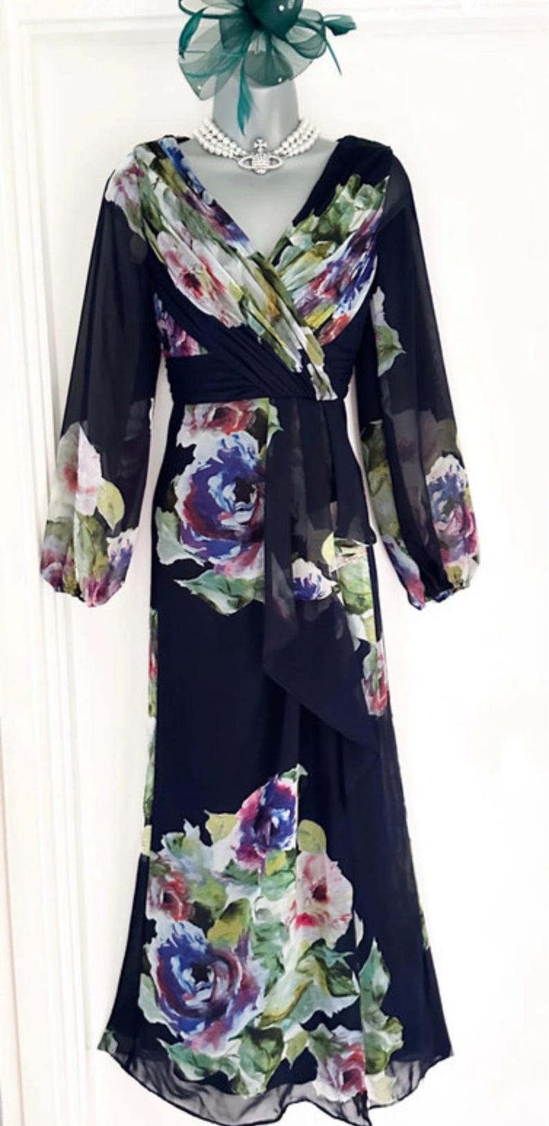Puede incluir: Vestido largo negro con estampado floral. Presenta mangas largas y escote en V. El dise&ntilde;o floral incluye tonos morados, azules, rosas y verdes. El vestido est&aacute; confeccionado con una tela ligera.
