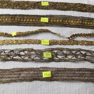 Puede incluir: Surtido de cintas decorativas doradas y marrones. Las cintas presentan varios diseños, incluyendo patrones florales y geométricos. Las medidas se indican en etiquetas amarillas en centímetros, con la cinta más larga de 58 cm.