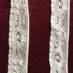Peut inclure: Deux morceaux de dentelle blanche avec un motif floral délicat. La dentelle est sur un fond rouge foncé.