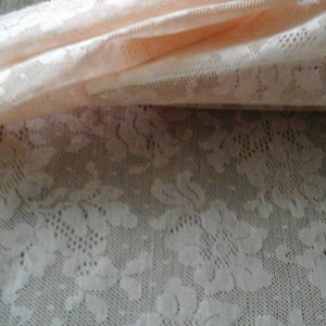 May include: Peach-coloured lace fabric with a floral pattern. The fabric is sheer and delicate, with a soft, feminine feel.
