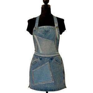 Peut inclure: Un tablier en jean avec un motif patchwork. Le tablier est fait de denim clair et moyen, avec des poches et un bavoir. Il est présenté sur un mannequin noir, mettant en valeur son style unique et artisanal.