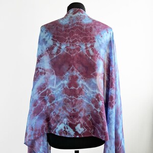 A light blue and purple silk scarf with a tie dye pattern. Hand painted blue marsala silk shawl. The scarf is draped over a black mannequin.