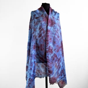 A light blue and purple silk scarf with a tie dye pattern. Hand painted blue marsala silk shawl. The scarf is draped over a black mannequin.