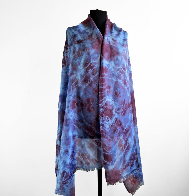 A light blue and purple silk scarf with a tie dye pattern. Hand painted blue marsala silk shawl. The scarf is draped over a black mannequin.