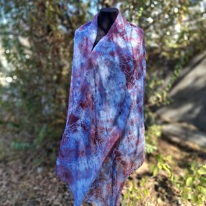 A light blue and purple silk scarf with a tie dye pattern. Hand painted blue marsala silk shawl. The scarf is draped over a black mannequin.
