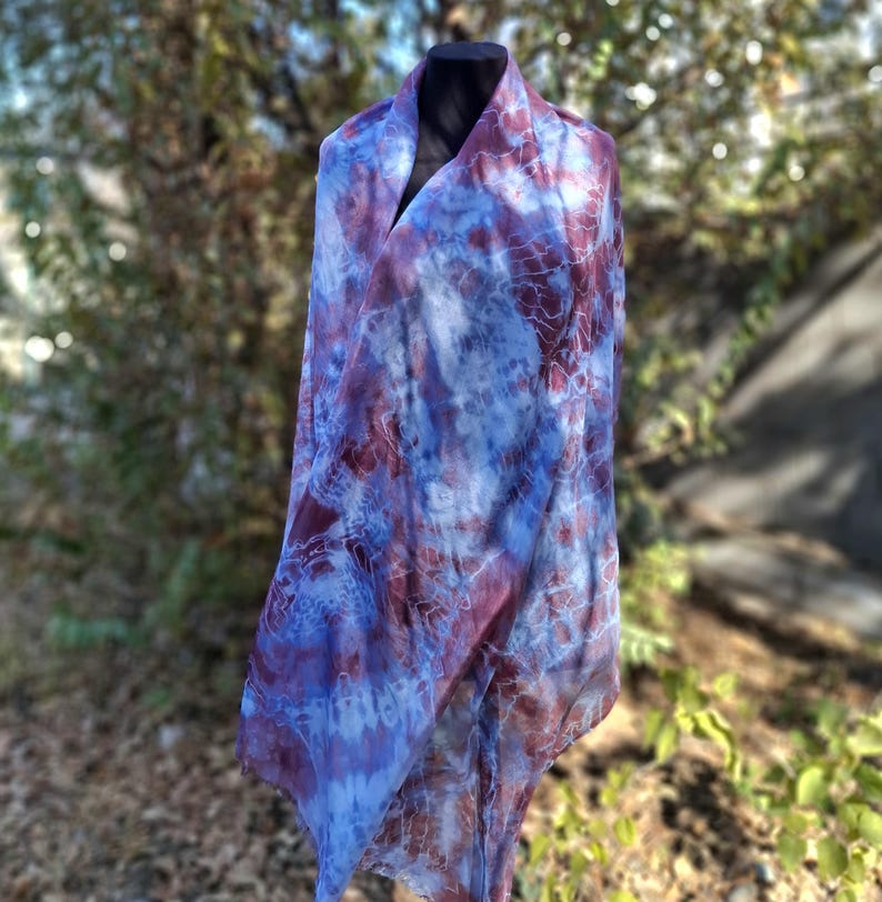 A light blue and purple silk scarf with a tie dye pattern. Hand painted blue marsala silk shawl. The scarf is draped over a black mannequin.
