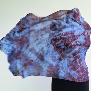 A light blue and purple silk scarf with a tie dye pattern. Hand painted blue marsala silk shawl. The scarf is draped over a black mannequin.