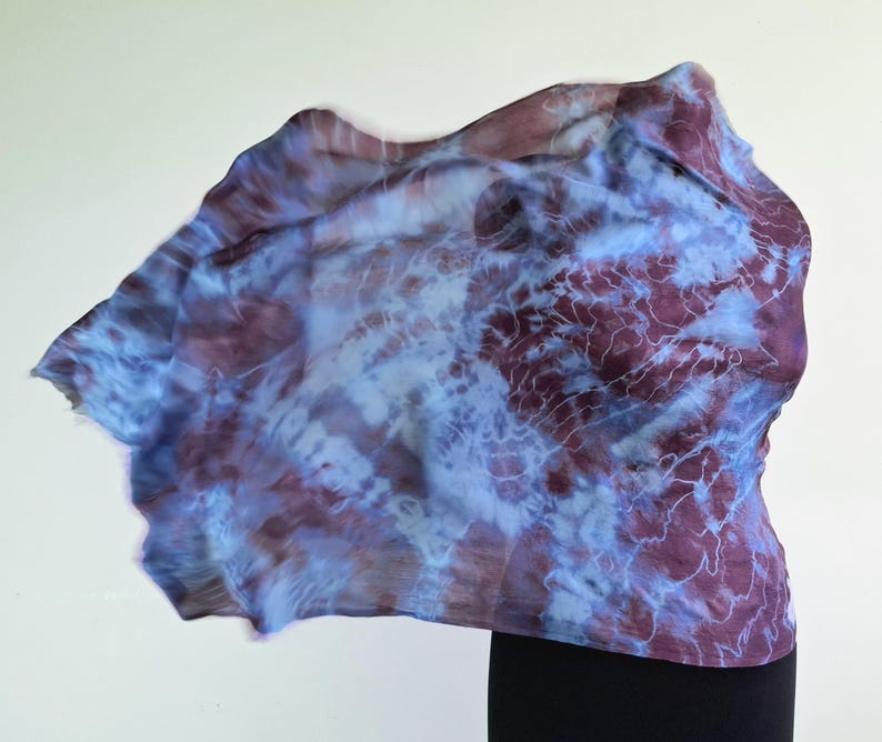 A light blue and purple silk scarf with a tie dye pattern. Hand painted blue marsala silk shawl. The scarf is draped over a black mannequin.