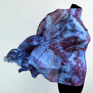 A light blue and purple silk scarf with a tie dye pattern. Hand painted blue marsala silk shawl. The scarf is draped over a black mannequin.