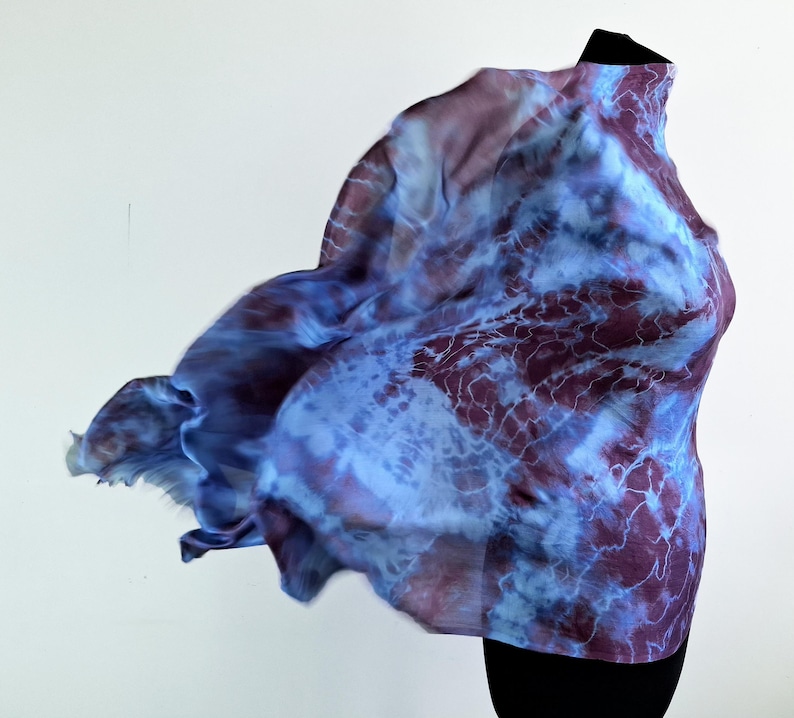 A light blue and purple silk scarf with a tie dye pattern. Hand painted blue marsala silk shawl. The scarf is draped over a black mannequin.