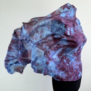 A light blue and purple silk scarf with a tie dye pattern. Hand painted blue marsala silk shawl. The scarf is draped over a black mannequin.
