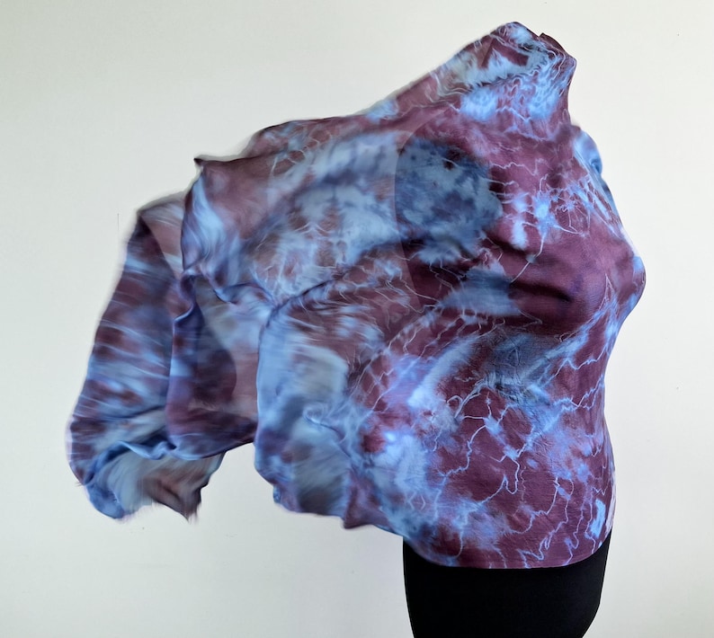A light blue and purple silk scarf with a tie dye pattern. Hand painted blue marsala silk shawl. The scarf is draped over a black mannequin.