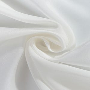 May include: Close-up of white fabric with soft folds and a silky texture. The fabric appears to be lightweight and flowing, with highlights and shadows creating depth. The overall impression is one of elegance and smoothness.