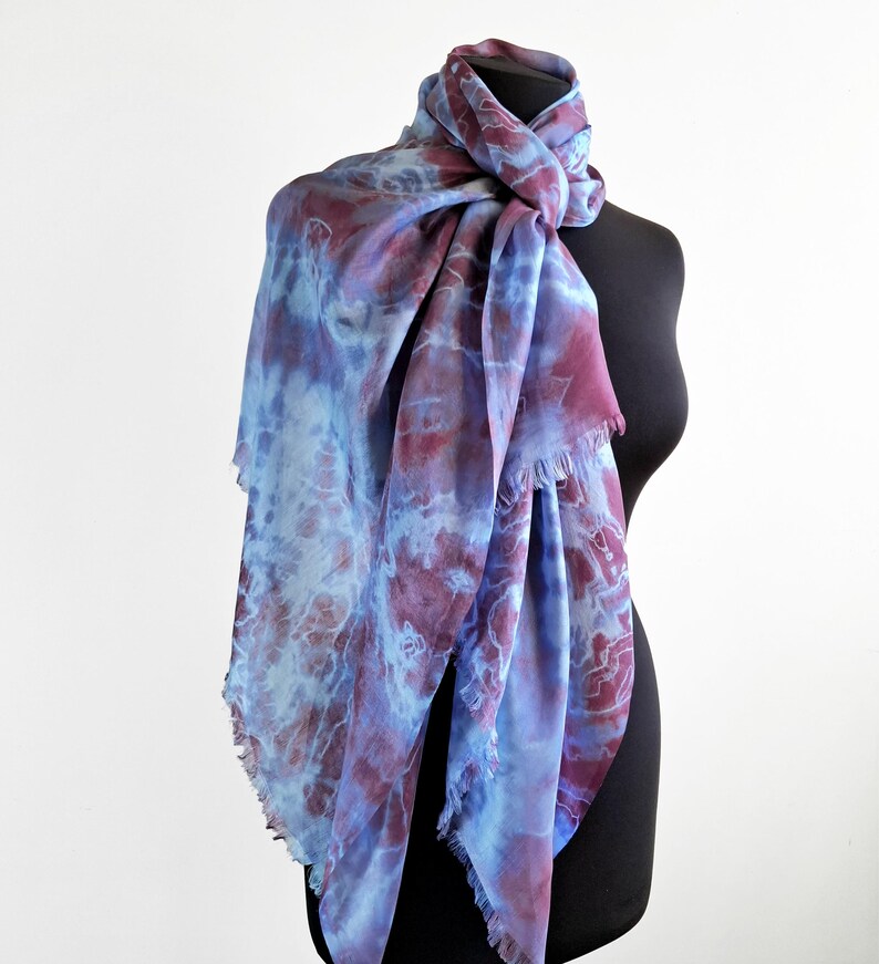 A light blue and purple silk scarf with a tie dye pattern. Hand painted blue marsala silk shawl. The scarf is draped over a black mannequin.