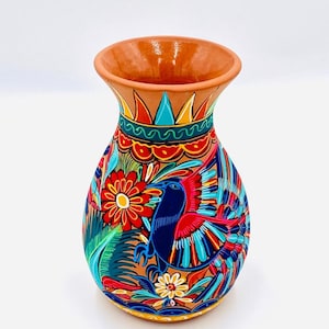 jarrón hecho de arcilla pintada a mano por indígenas mexicanos en colores brillantes con dibujos de flores, pavos reales, smong otros.