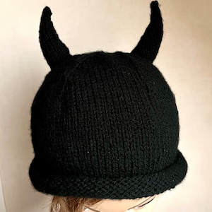 Peut inclure: Chapeau noir en tricot avec deux cornes sur le dessus. Le chapeau est fait d'un matériau doux et chaud et a une texture côtelée.